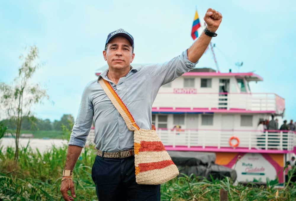 Director del DNP Alexander Lopez,    con el brazo derecho arriba, en señal de Victoria. De fondo una barca en el río Amazonas.